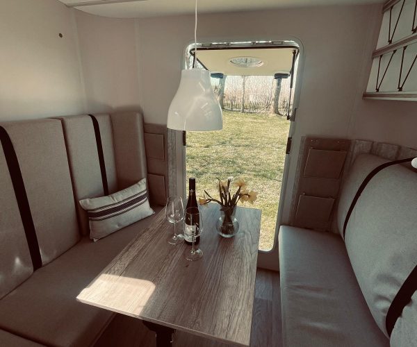 Heller und einladender Innenraum eines Wohnwagens, der eine Essecke mit zwei gegenüberliegenden Sitzbänken und einem Holztisch zeigt.